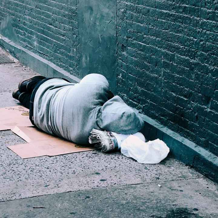 Turned away from the camera, a person sleeps on the street next to a brick wall