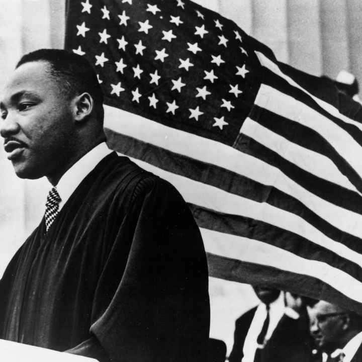 Black and White Photo shows Dr. Martin Luther King Jr. in front of an American flag