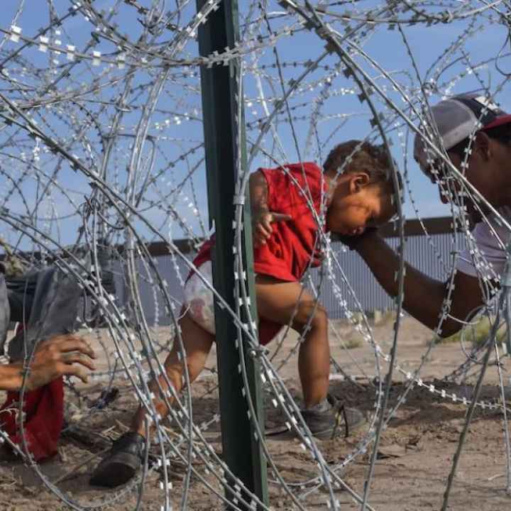 A young child in a red shirt tries to make their way through razor wire.