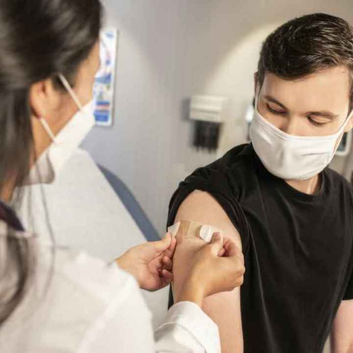 A person wearing a mask is given a shot by a doctor. 