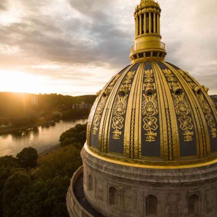 AN aerial shot of the WV Capitol's gold dome while the sun sets over the Kanawha River